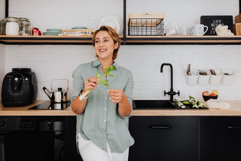 Smiling woman with vegetables in a stylish kitchen showcasing modern interior design.